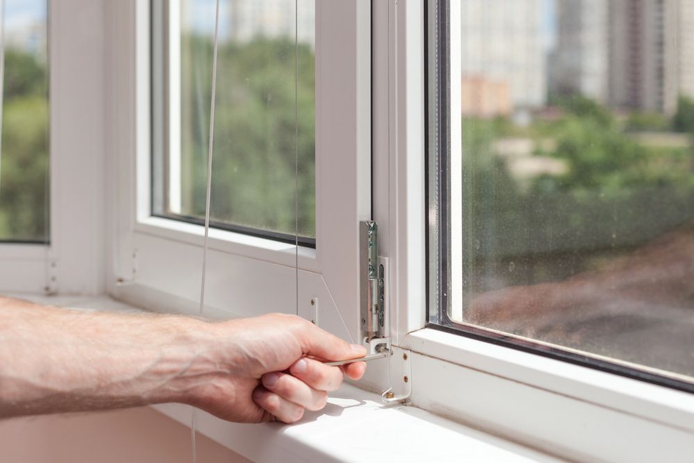 Apretando a mano el pestillo de una ventana con marco blanco y vista exterior borrosa.