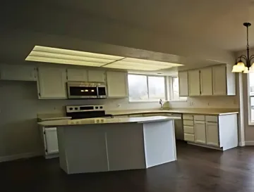 Ellis & Son Painting - An empty kitchen with white cabinets and a large island