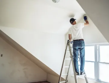 Ellis & Son Painting - A man is standing on a ladder painting a wall.