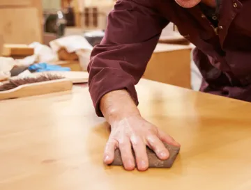 Ellis & Son Painting - A man is sanding a wooden table with a sanding block.