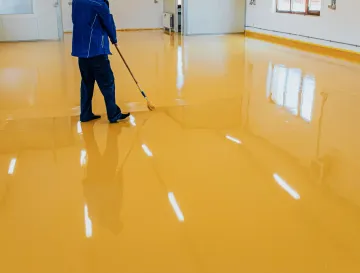 Ellis & Son Painting - A man is painting a yellow floor with a roller.