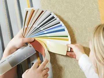 Ellis & Son Painting - A woman is holding a fan of paint samples in front of a wall.