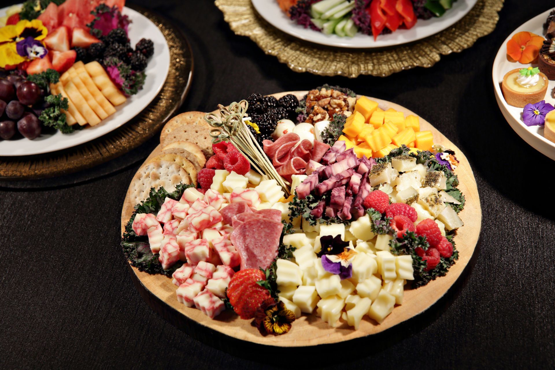 A plate of food with meat , cheese , fruit and vegetables on a table.