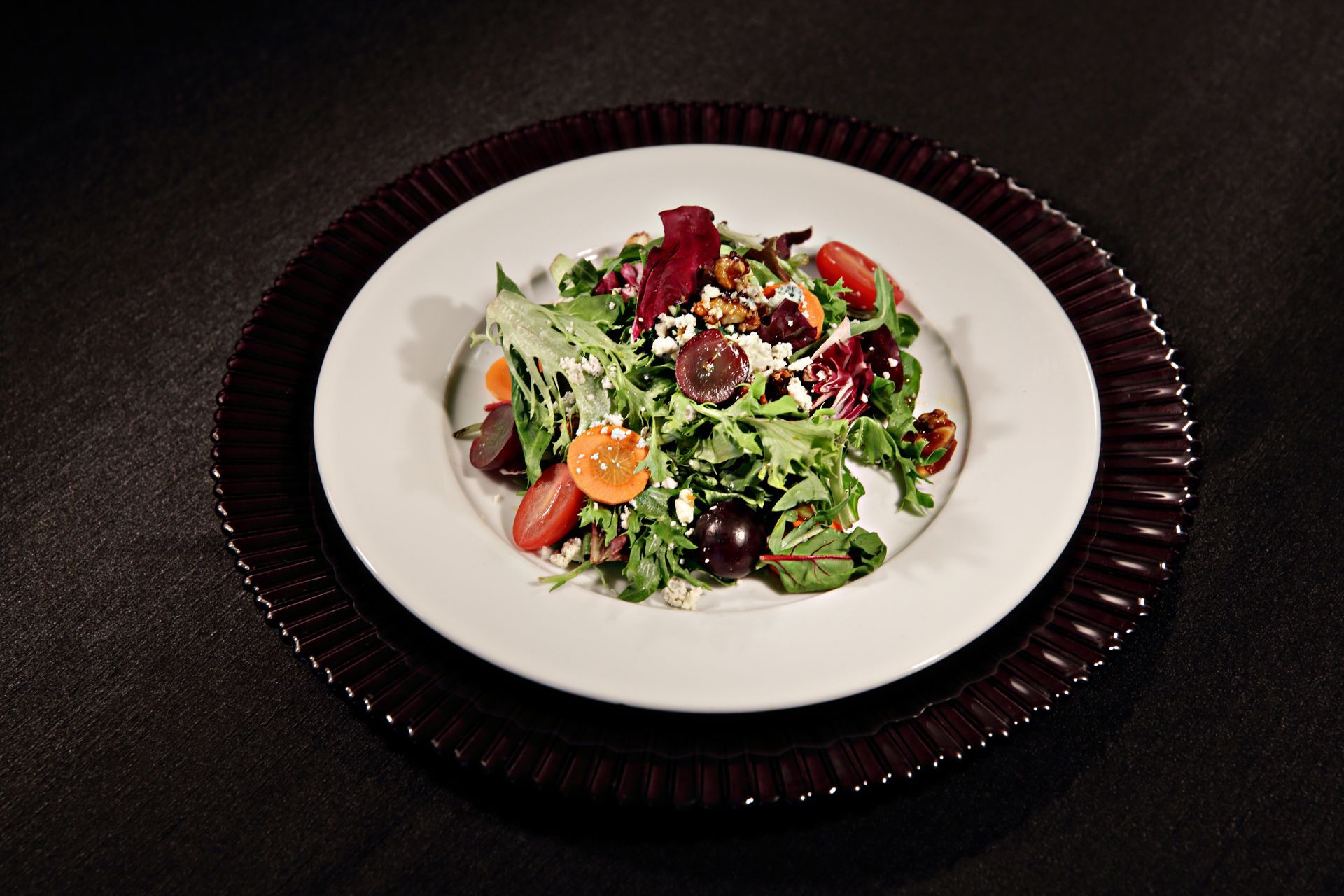 A white plate topped with a salad on a black plate