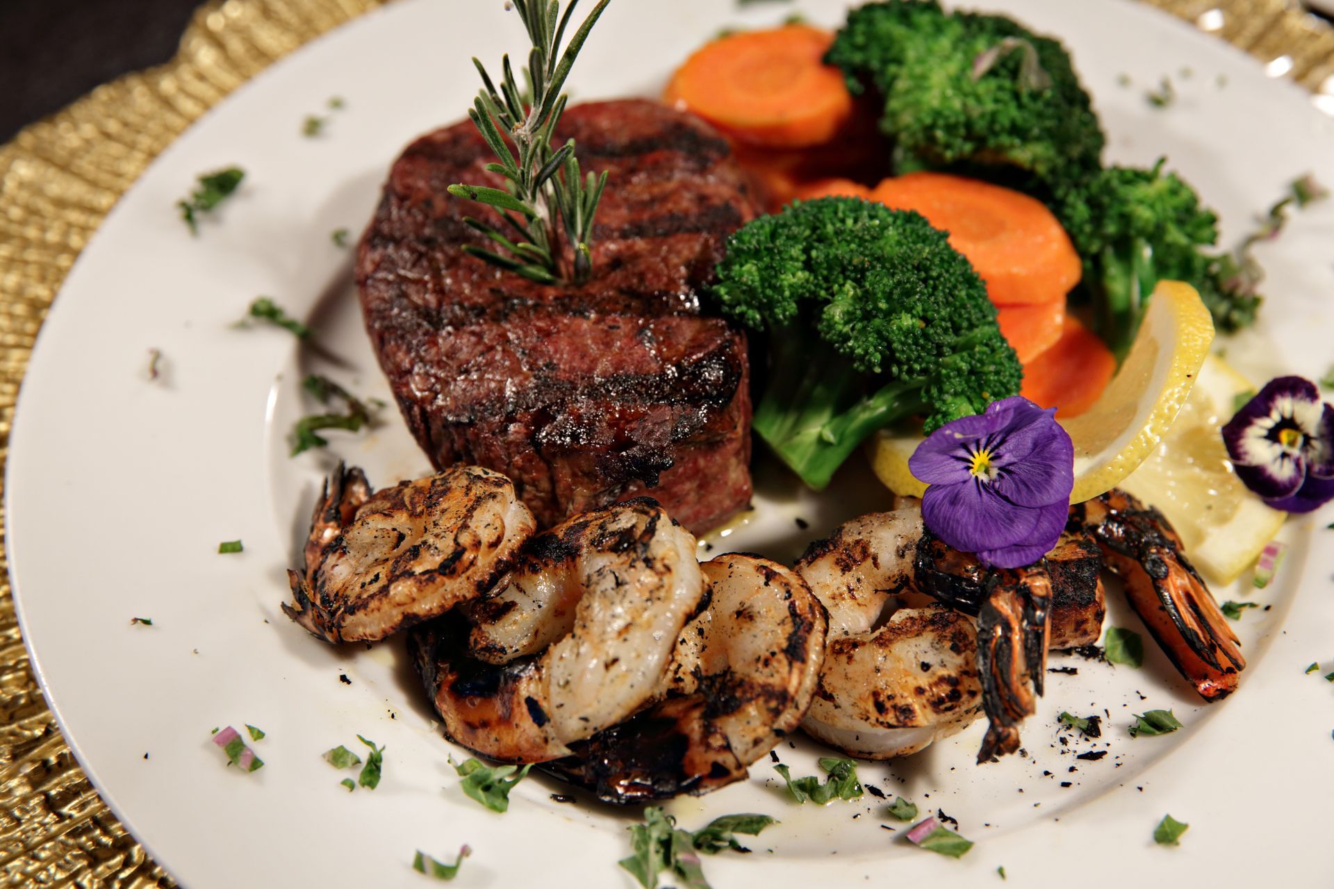 A white plate topped with a steak , shrimp , broccoli and carrots.