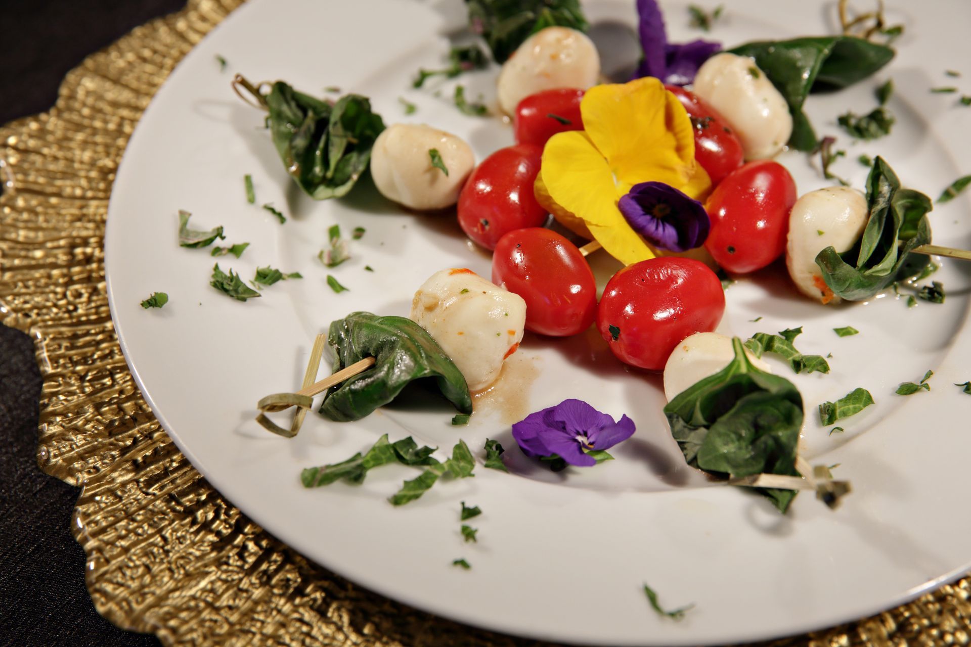 A white plate topped with tomatoes , mozzarella and spinach on skewers.