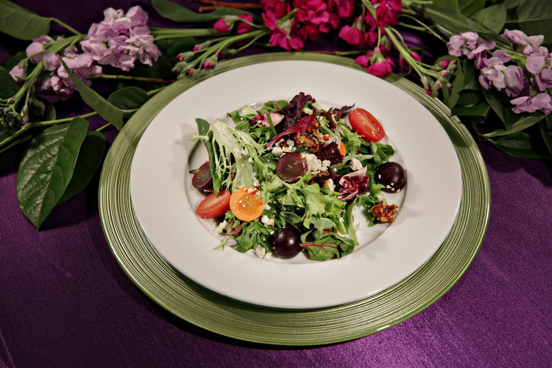 A salad on a green plate with flowers in the background