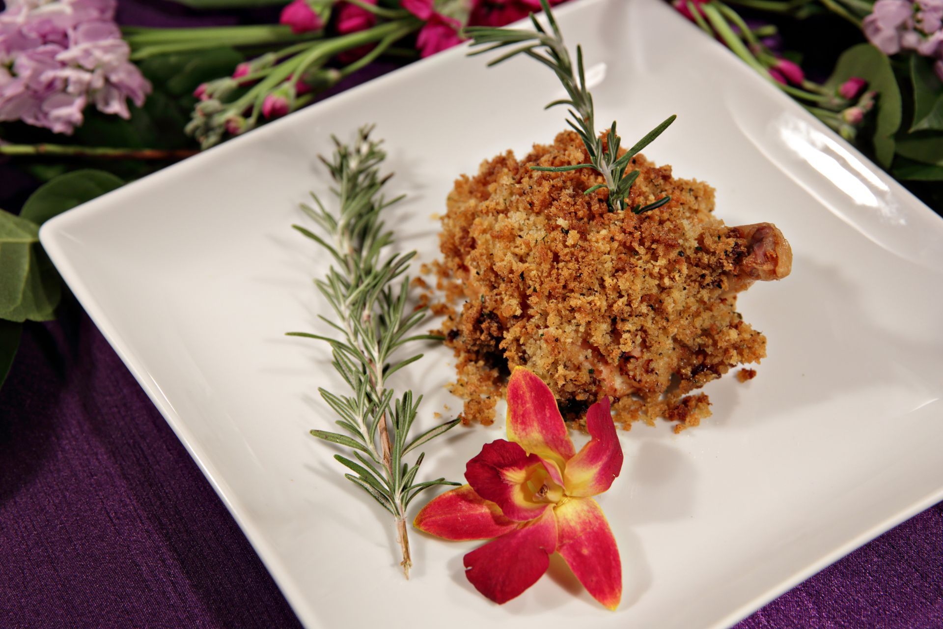 A plate of food with rosemary and a flower on it