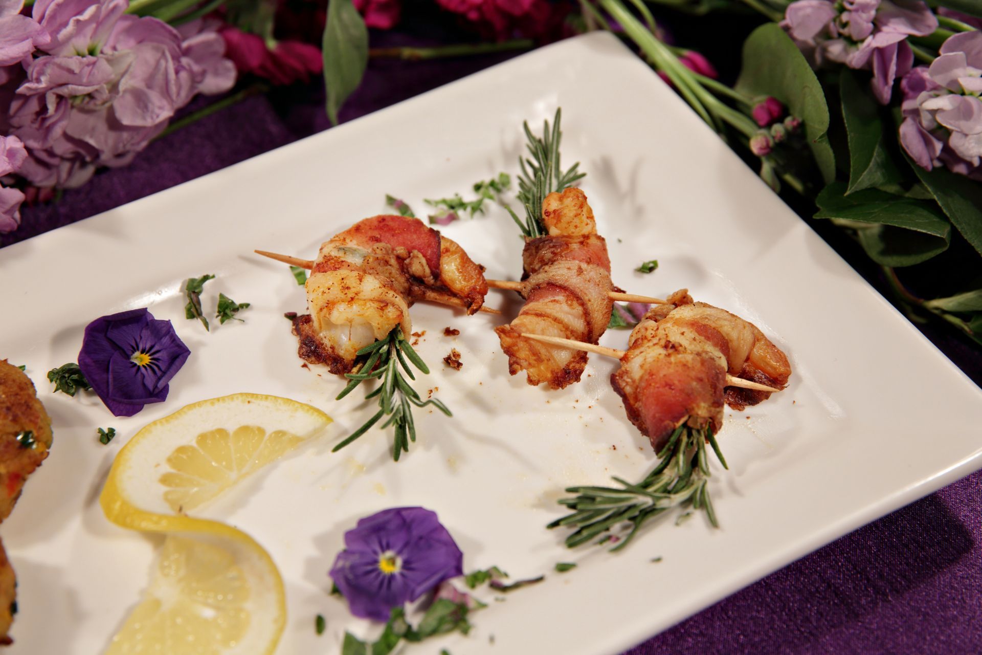 A white plate topped with shrimp wrapped in bacon and lemon slices
