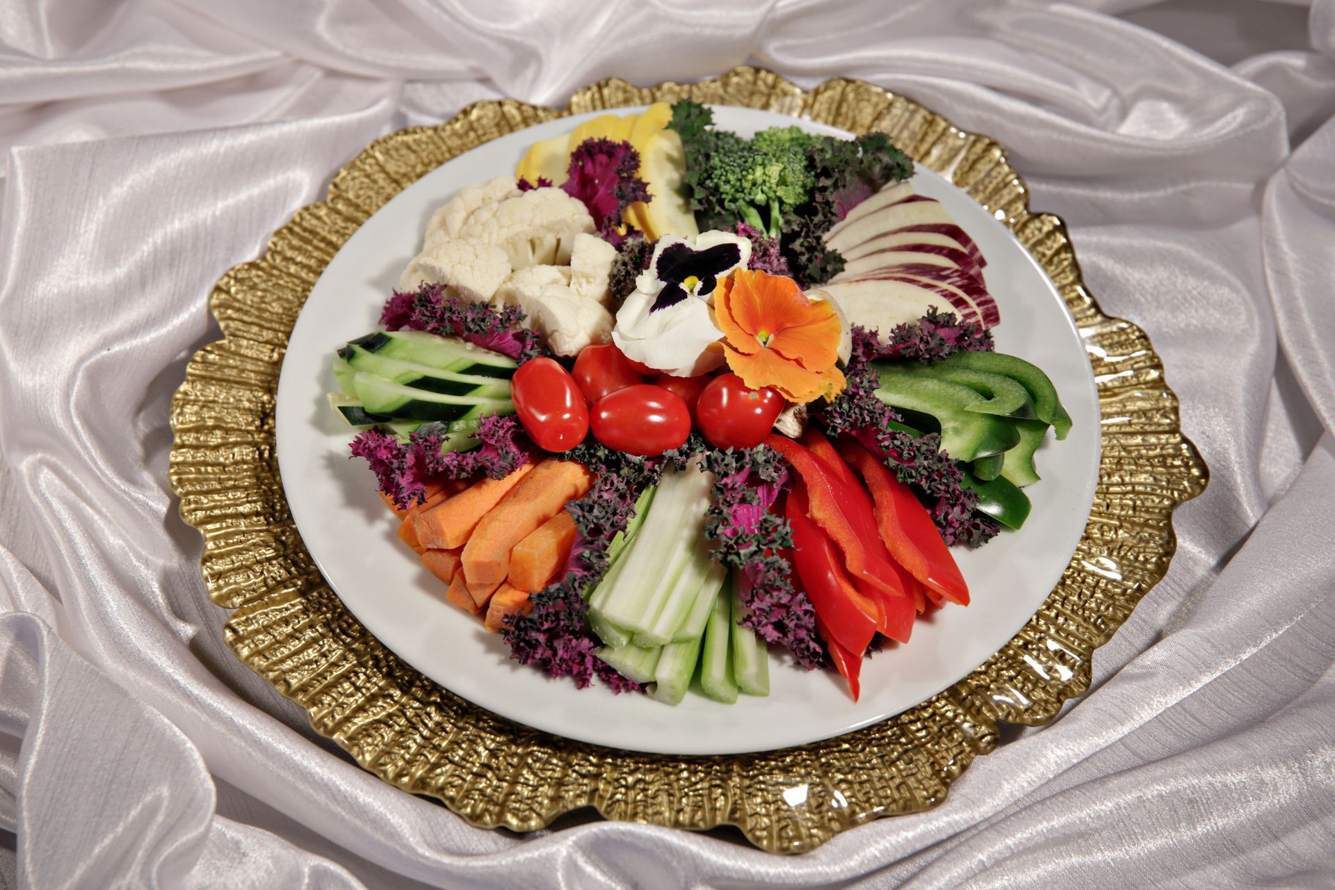 A plate of vegetables on a gold plate on a white cloth