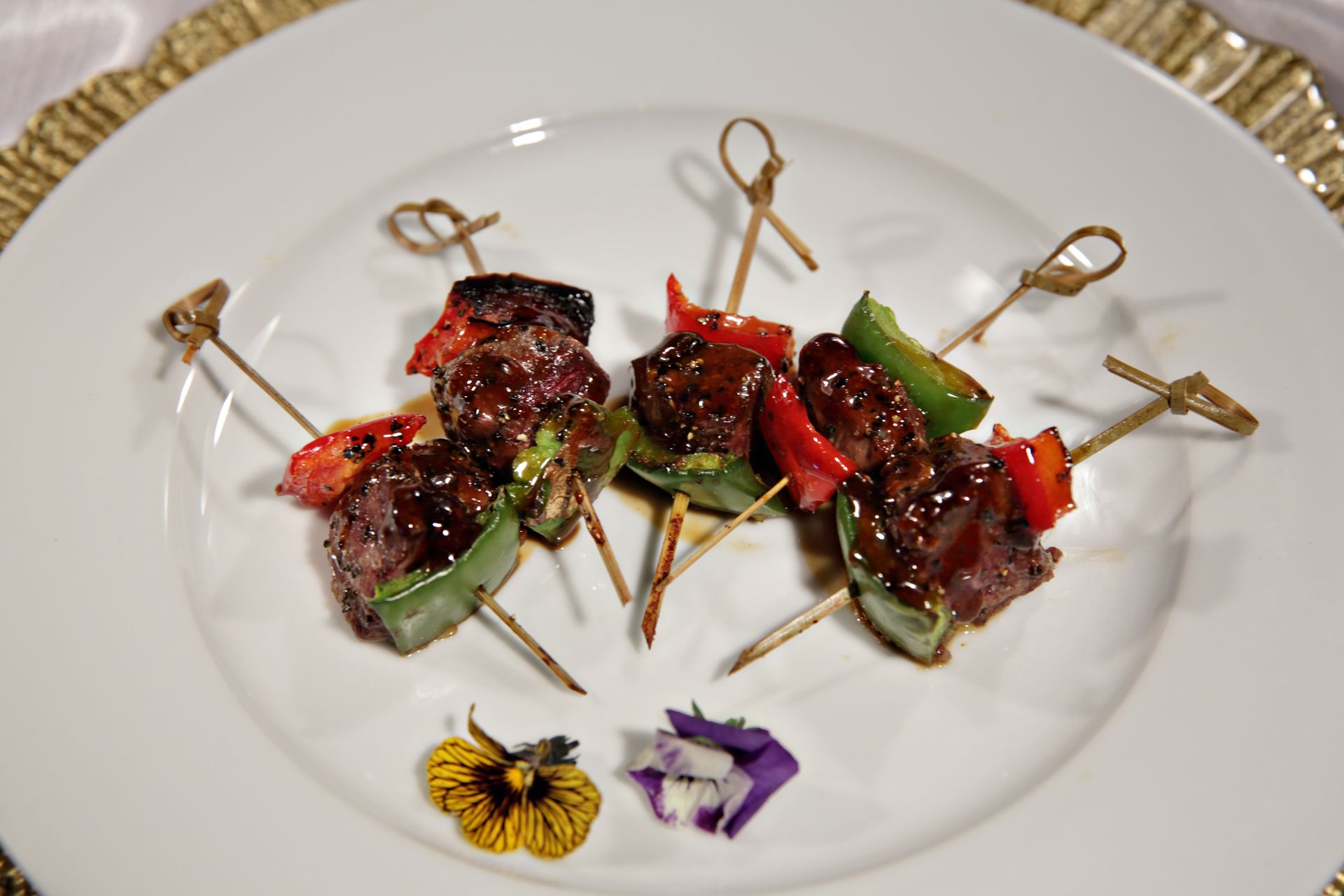 A white plate topped with skewers of meat and vegetables