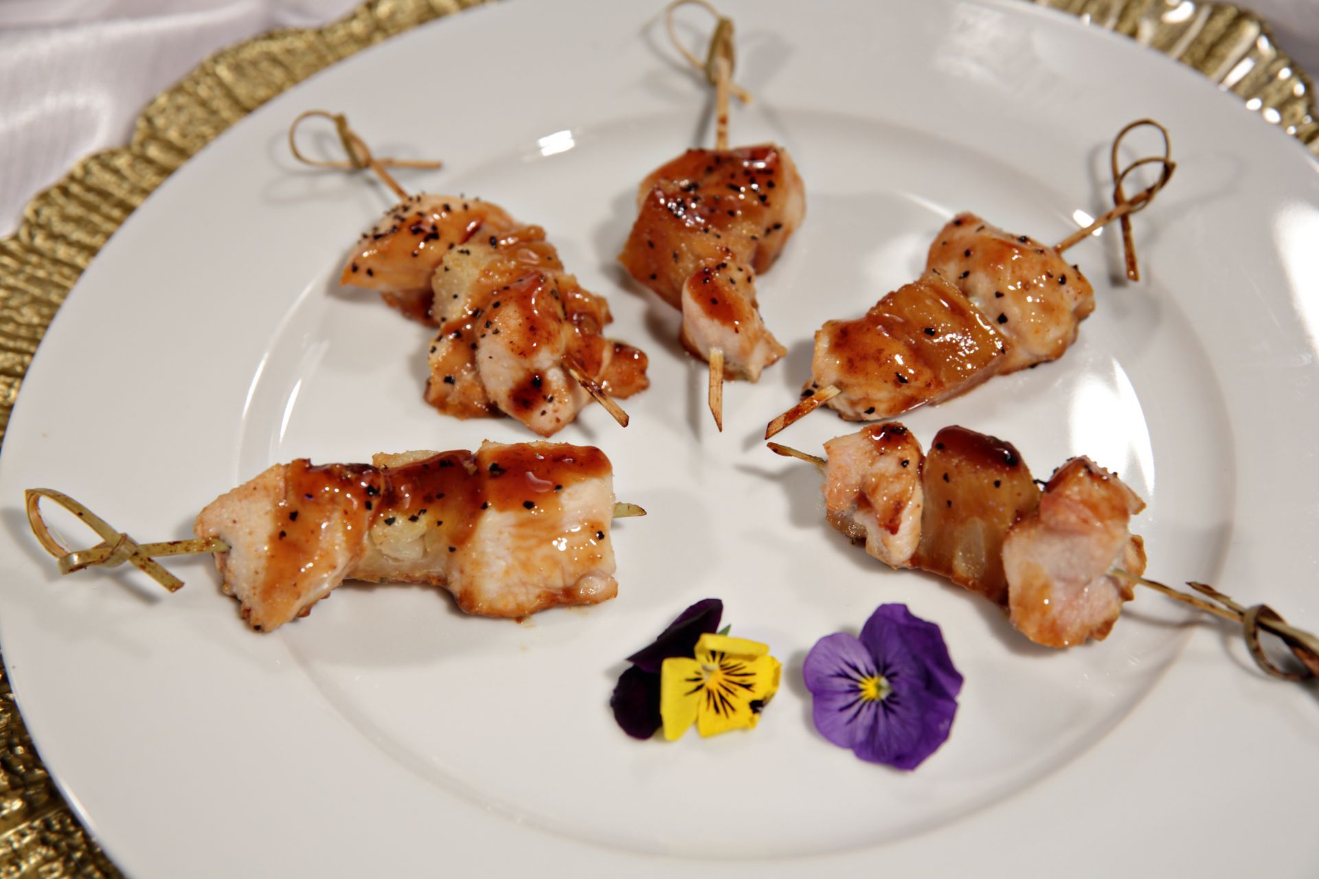 A white plate topped with chicken skewers and flowers