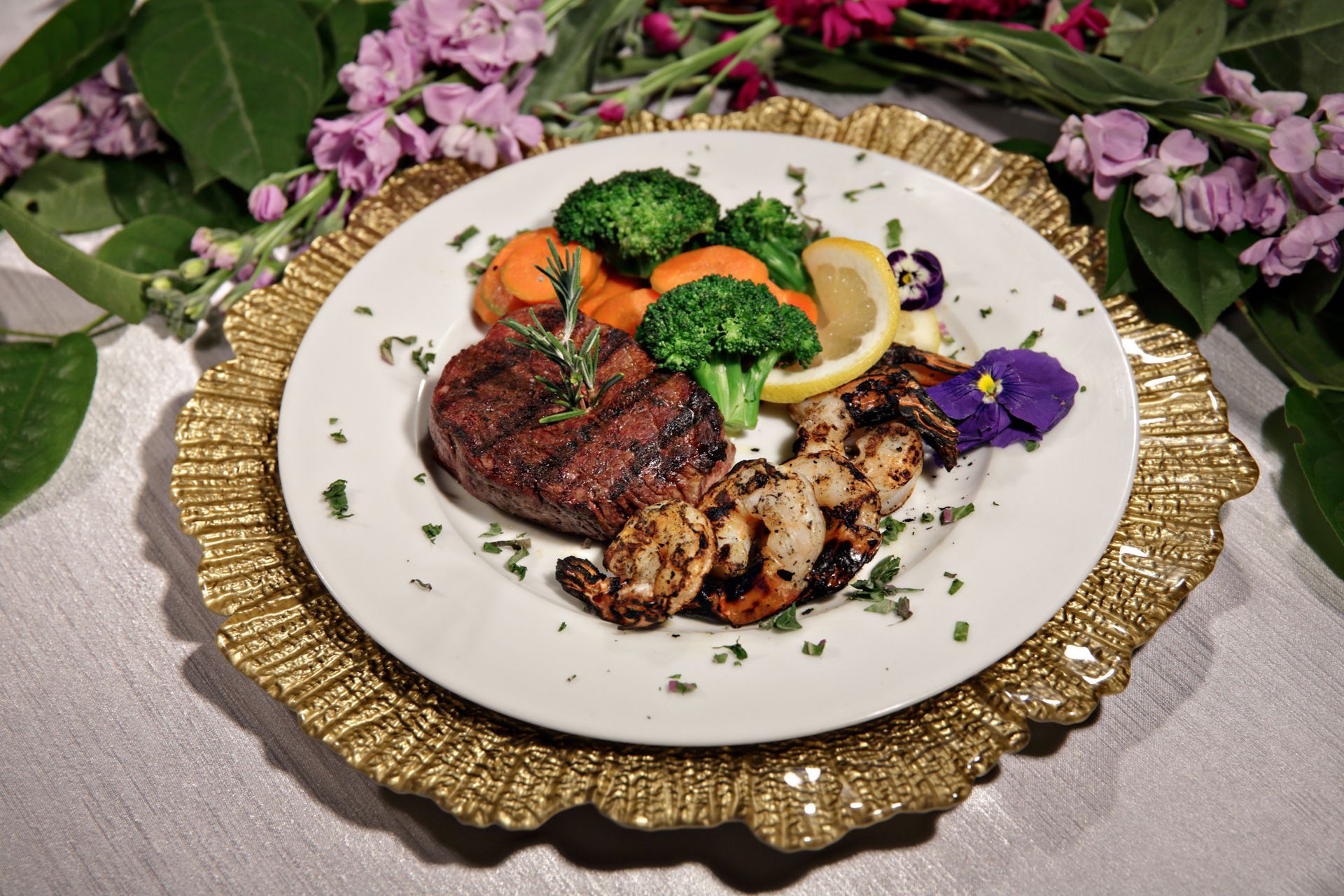 A plate of food with steak , shrimp , broccoli and carrots on a gold plate.