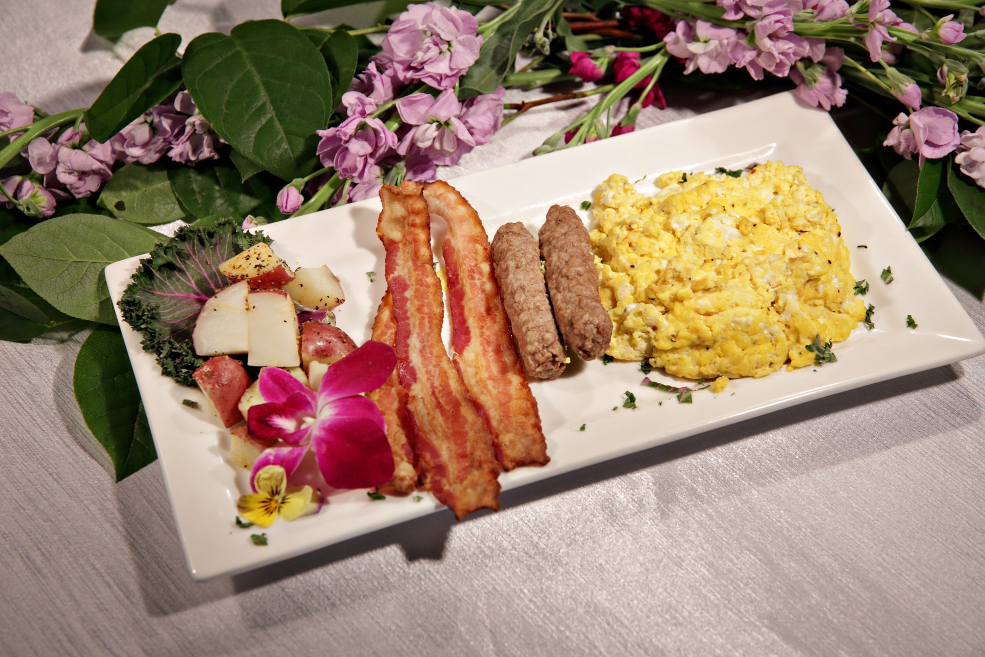 A white plate topped with bacon eggs and sausages