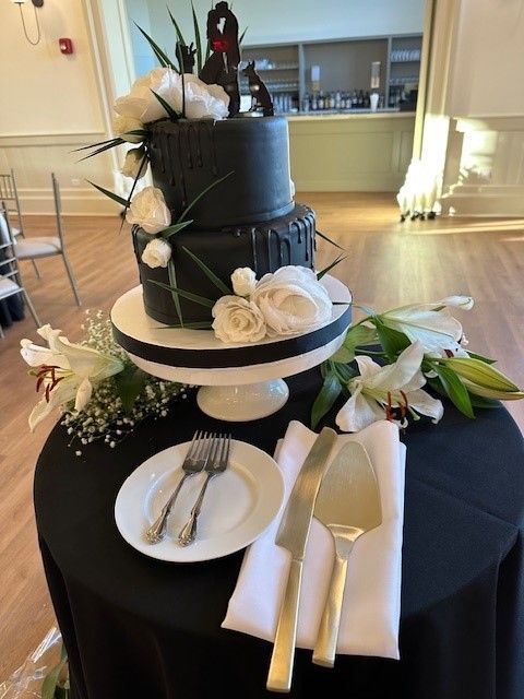 A black wedding cake is on a table with plates and silverware