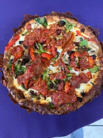 A pizza with pepperoni and vegetables on a purple table cloth.