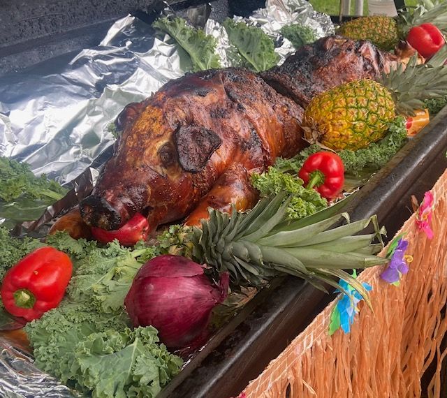 A roasted pig is surrounded by vegetables including pineapples and red peppers