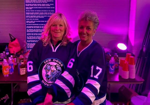 Two women wearing ice dogs hockey jerseys are posing for a picture.