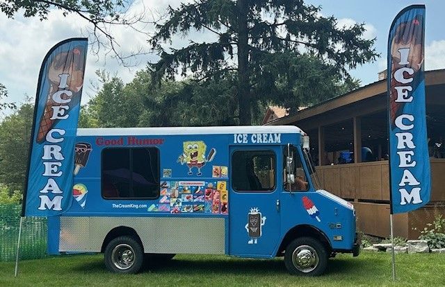 A blue and white ice cream truck is parked in a grassy field.