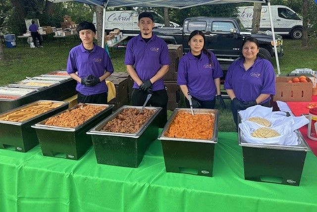 A group of people standing around a table with trays of food.