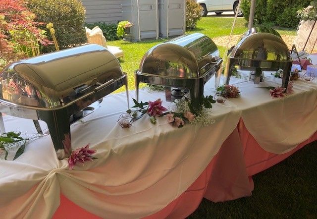 A buffet table with stainless steel containers and flowers on it.