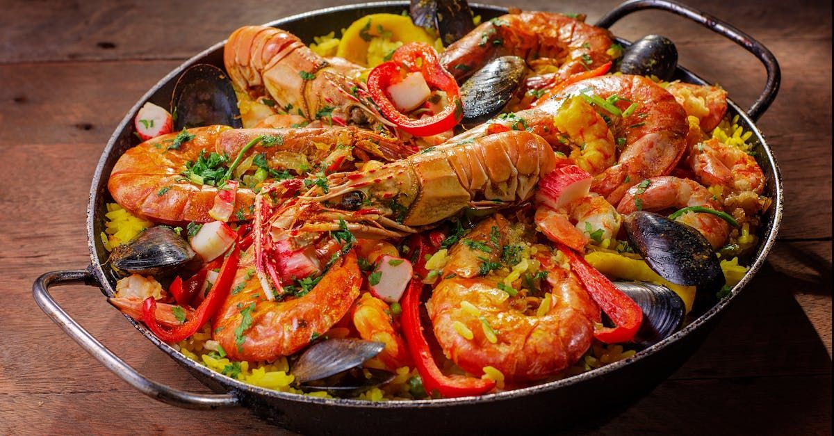 A pan filled with shrimp , mussels , peppers and rice on a wooden table.