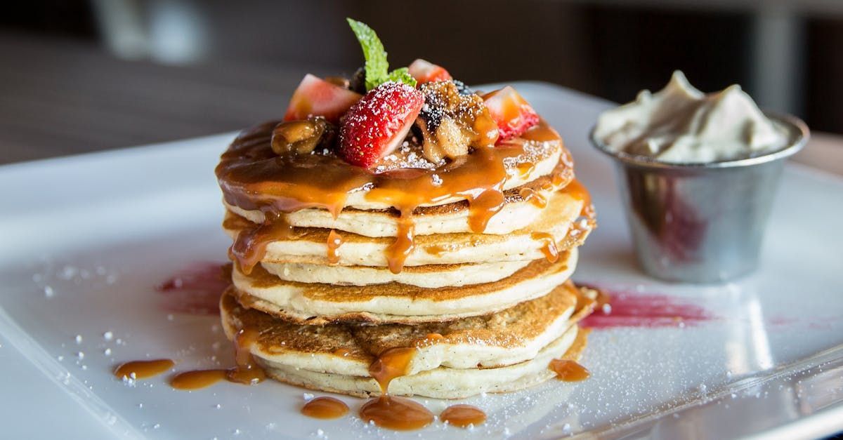 A stack of pancakes with strawberries and whipped cream on a white plate.