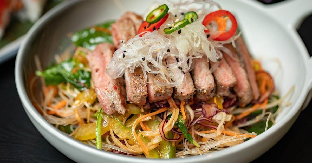 A close up of a bowl of food with meat and vegetables on a table.