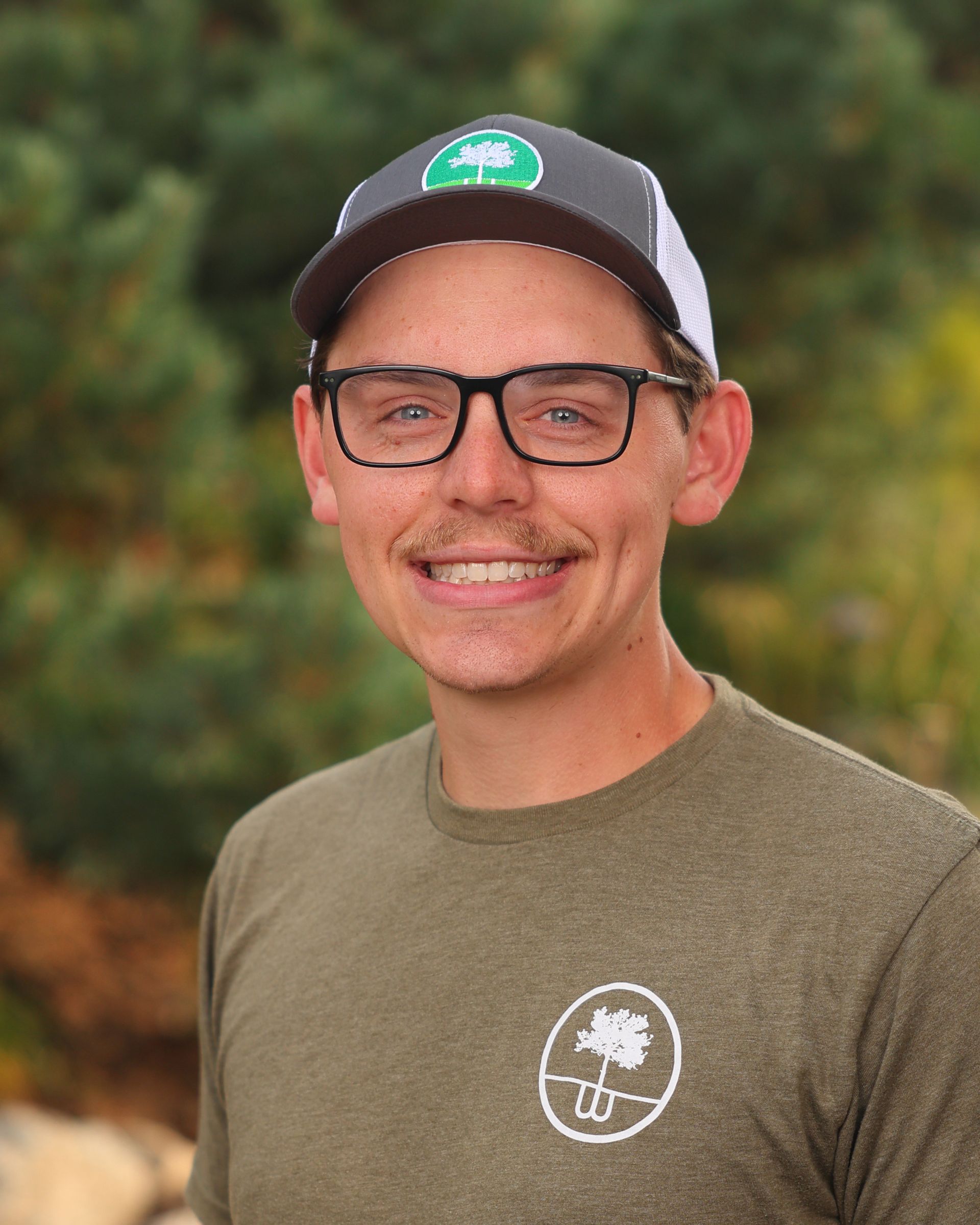 A man wearing glasses and a hat is smiling for the camera