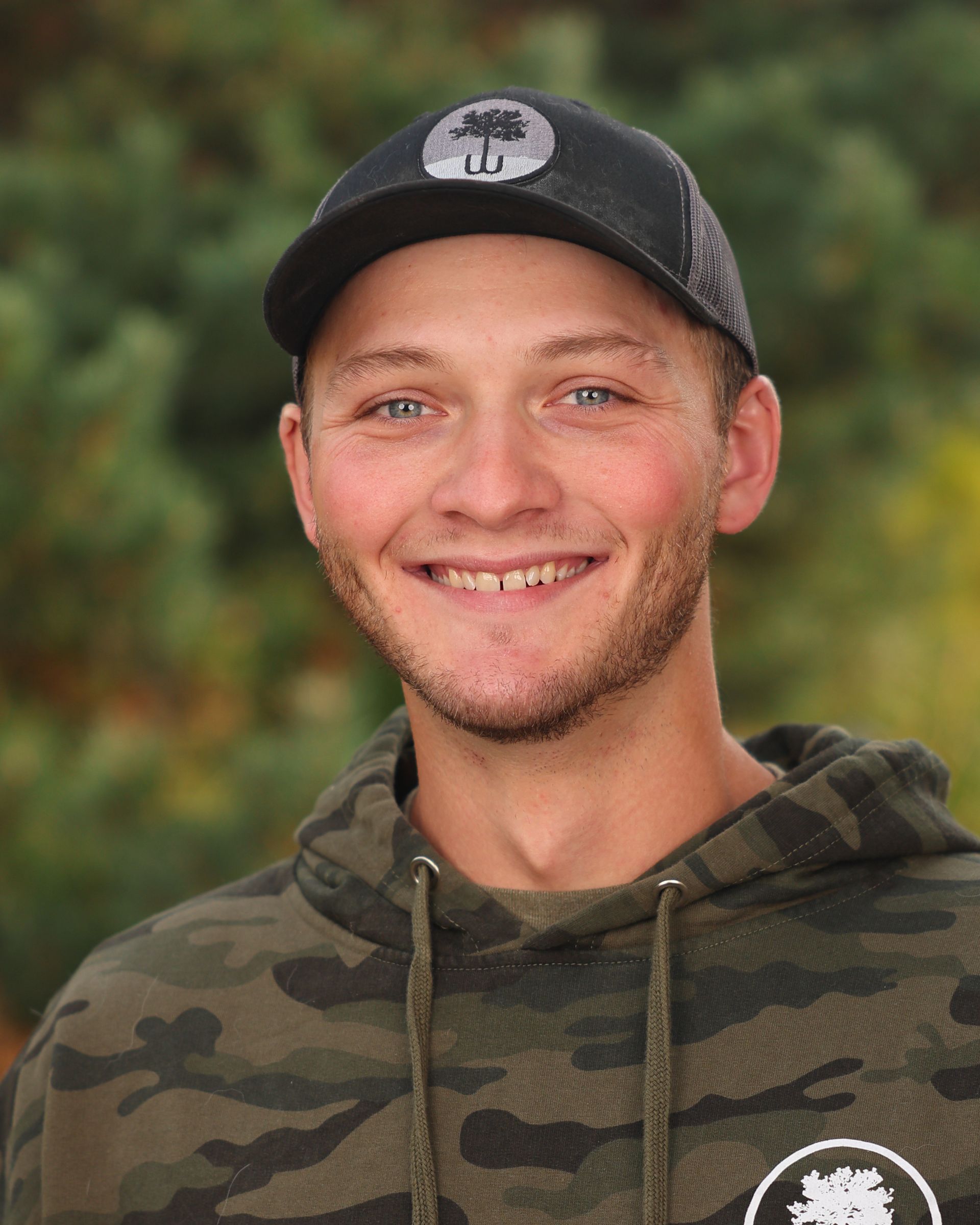 A man wearing a hat and a camouflage hoodie smiles for the camera