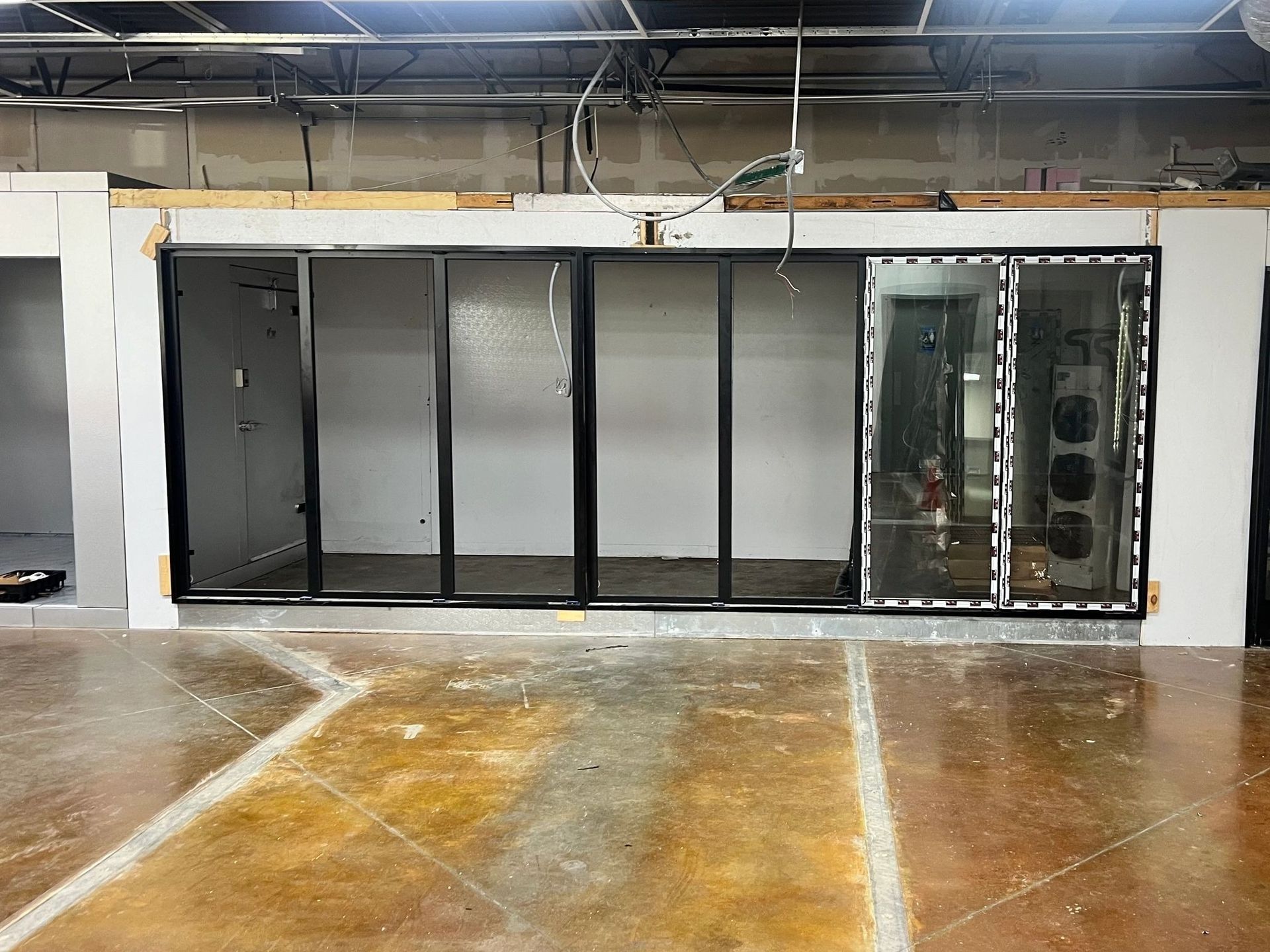 Interior construction site, exposed metal frames, glass and metal panels, concrete floor.