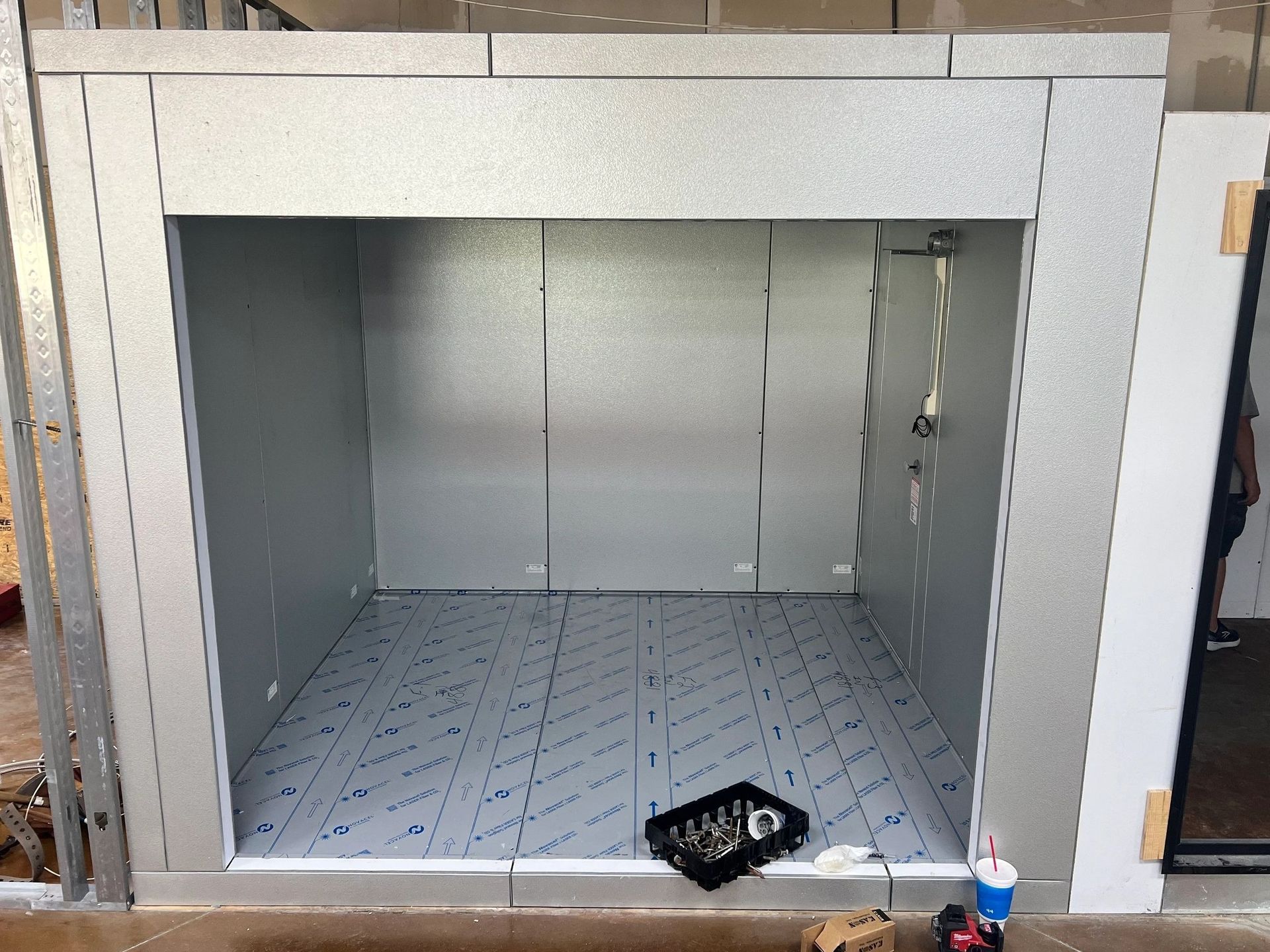 An empty, silver-walled elevator shaft with a patterned floor, under construction.