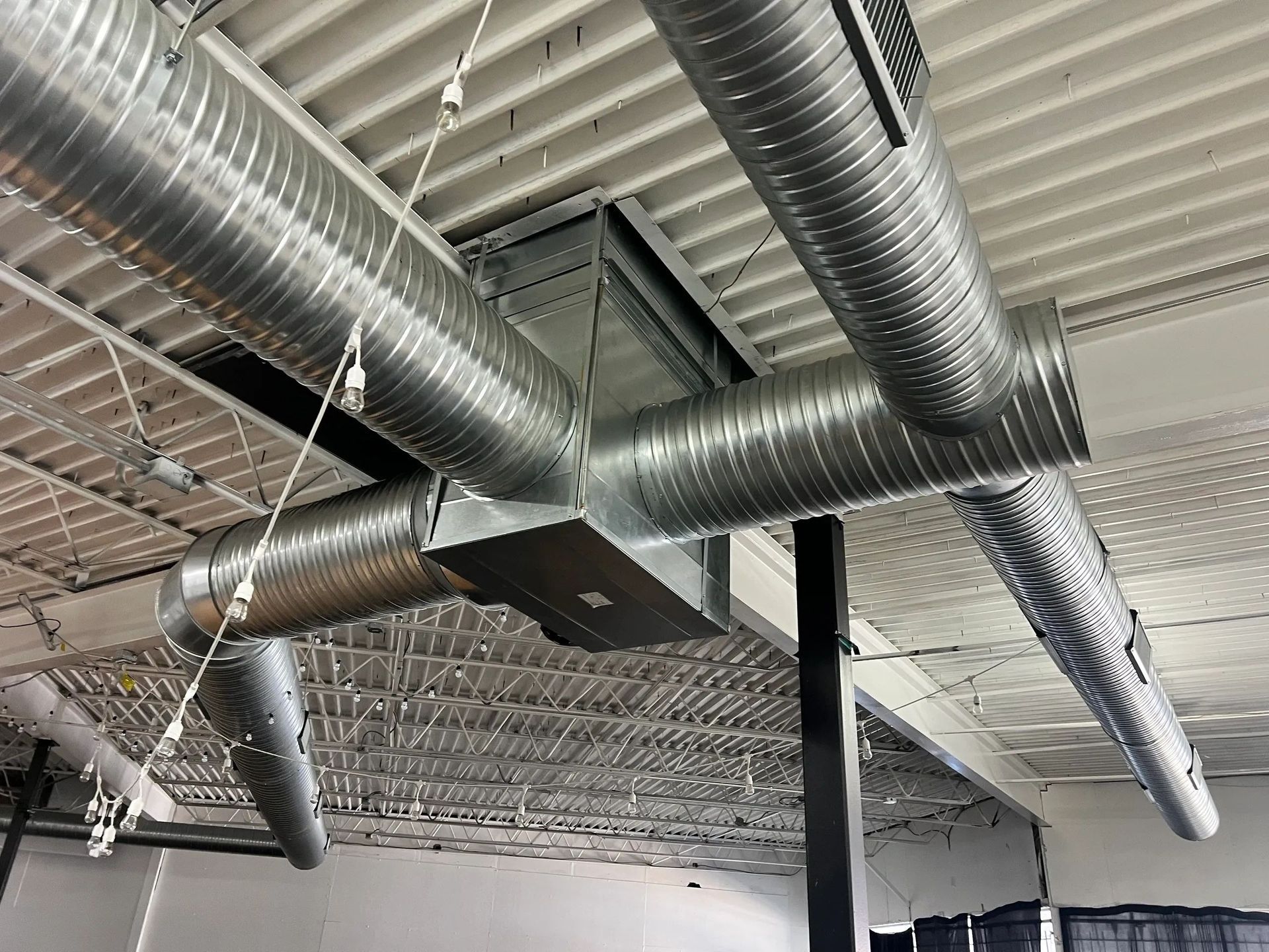Metal HVAC ductwork, attached to a white corrugated ceiling in a building.