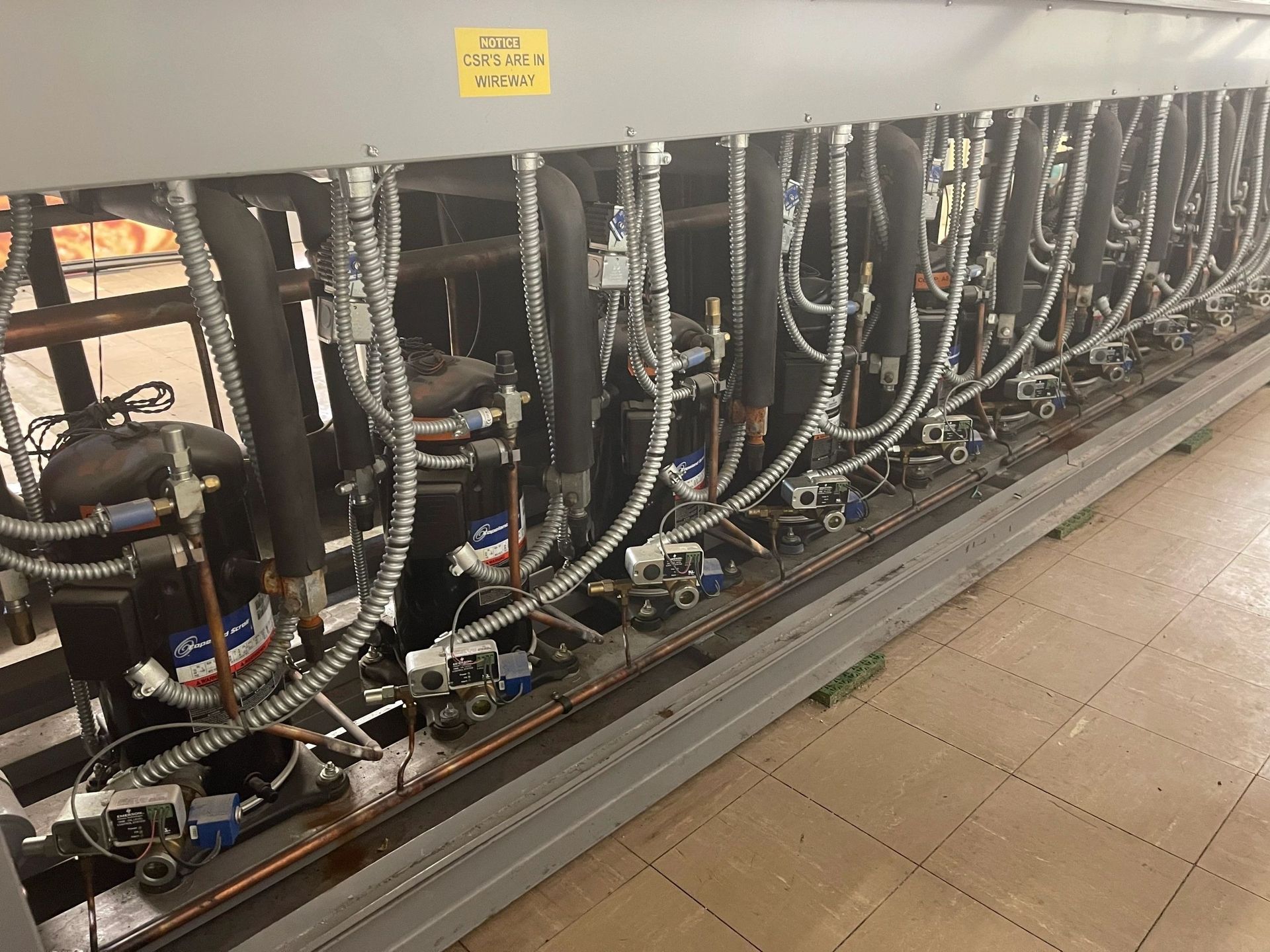 Industrial chiller with many pipes, valves, and a compressor, indoors.