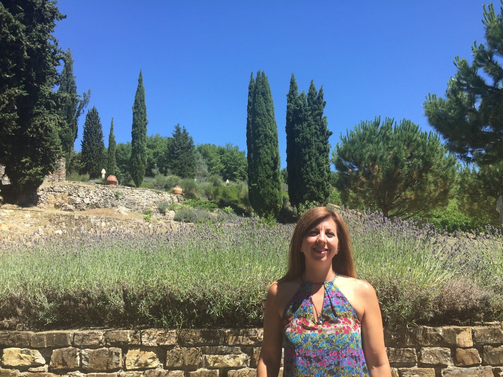 A woman is standing in front of a stone wall in a field of lavender.