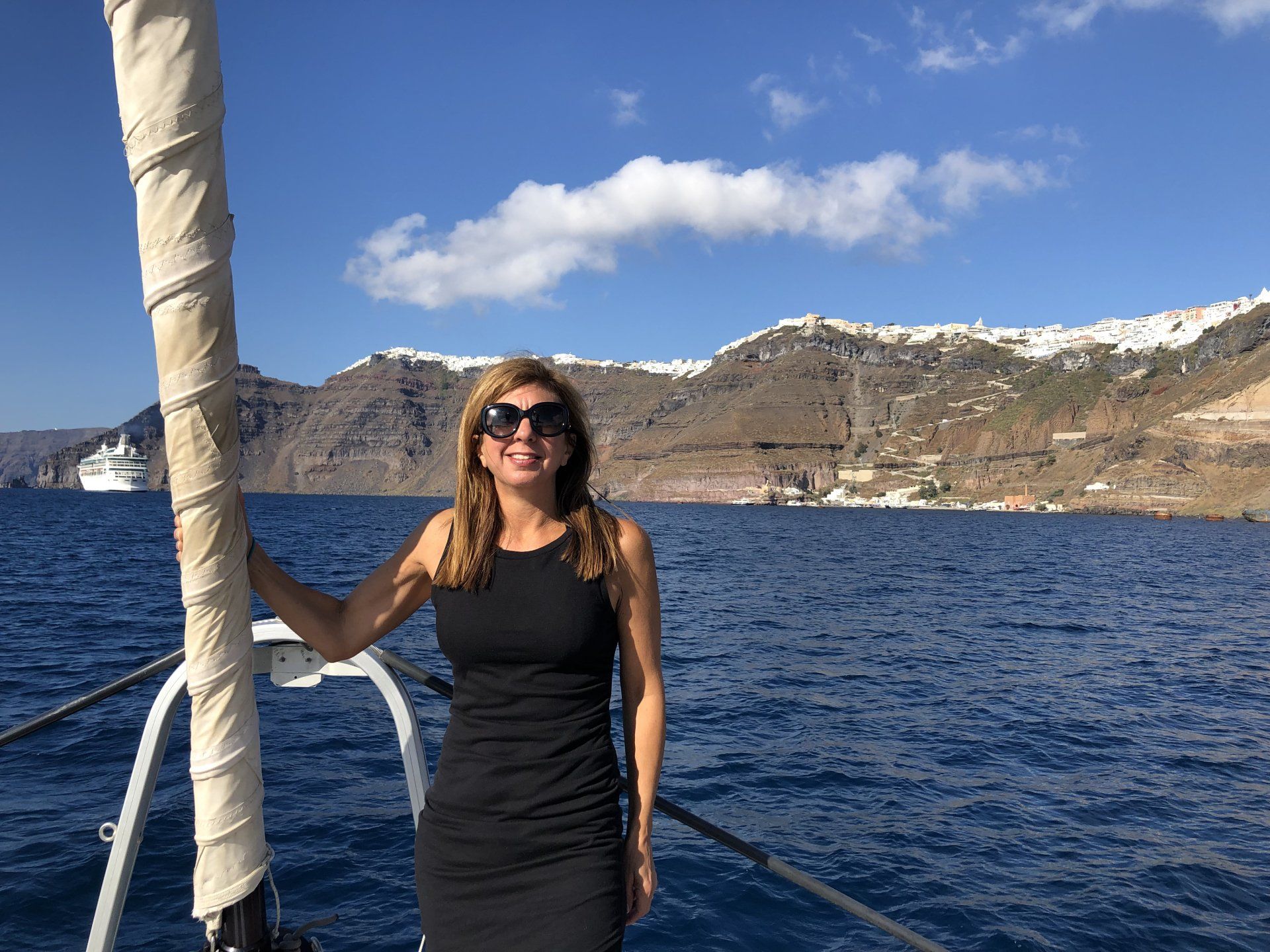 A woman in a black dress is standing on a boat in the ocean.