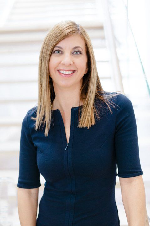 A woman in a blue dress is smiling and standing in front of a set of stairs.