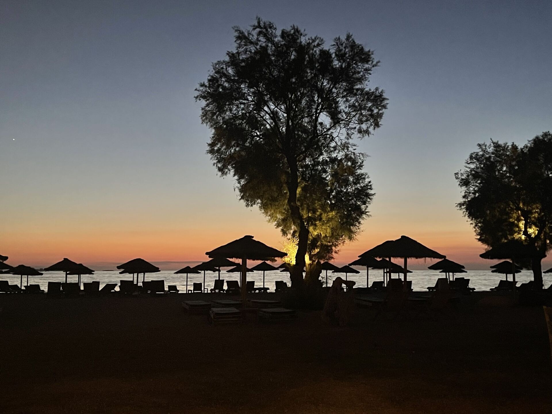 A sunset on a beach with umbrellas and chairs