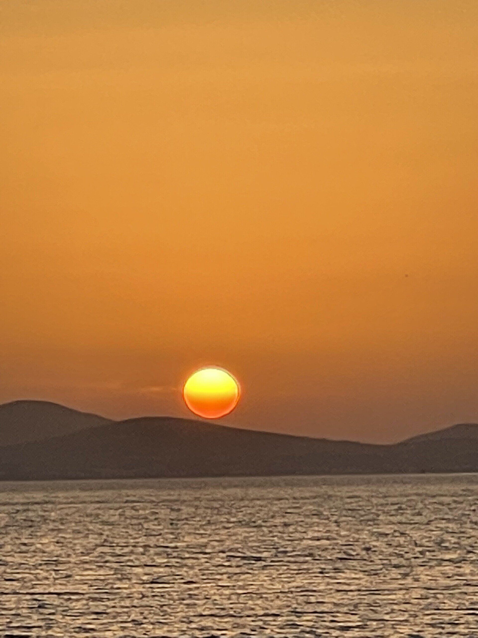 The sun is setting over the ocean with mountains in the background.