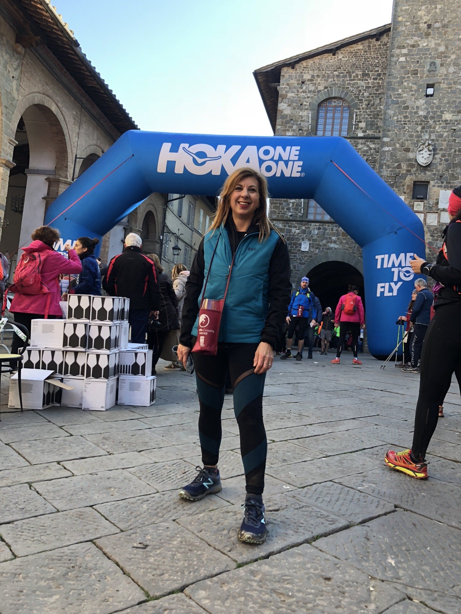 A woman is standing in front of a hoka one one inflatable arch.