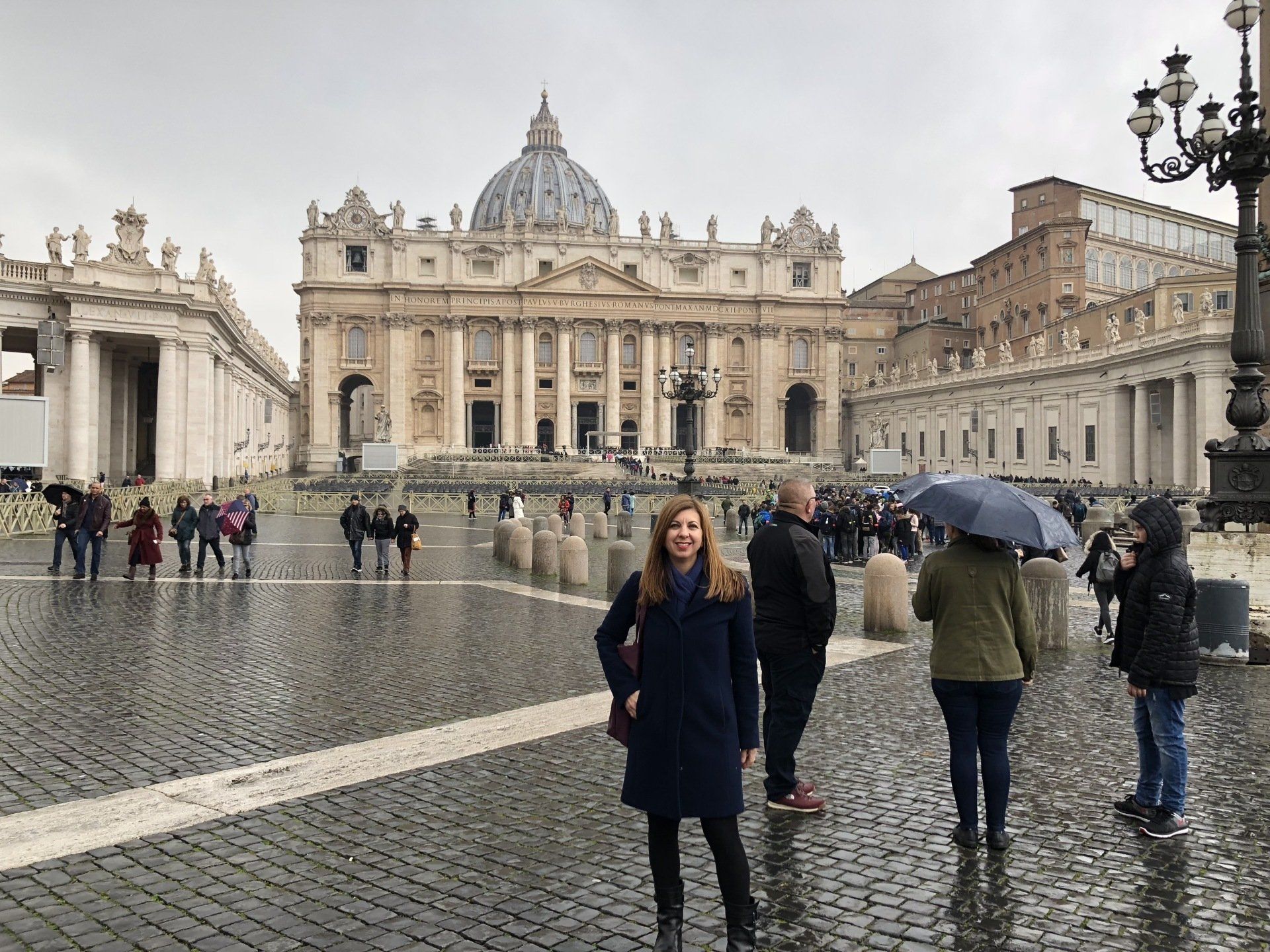 A woman is standing in front of a large building in the rain.