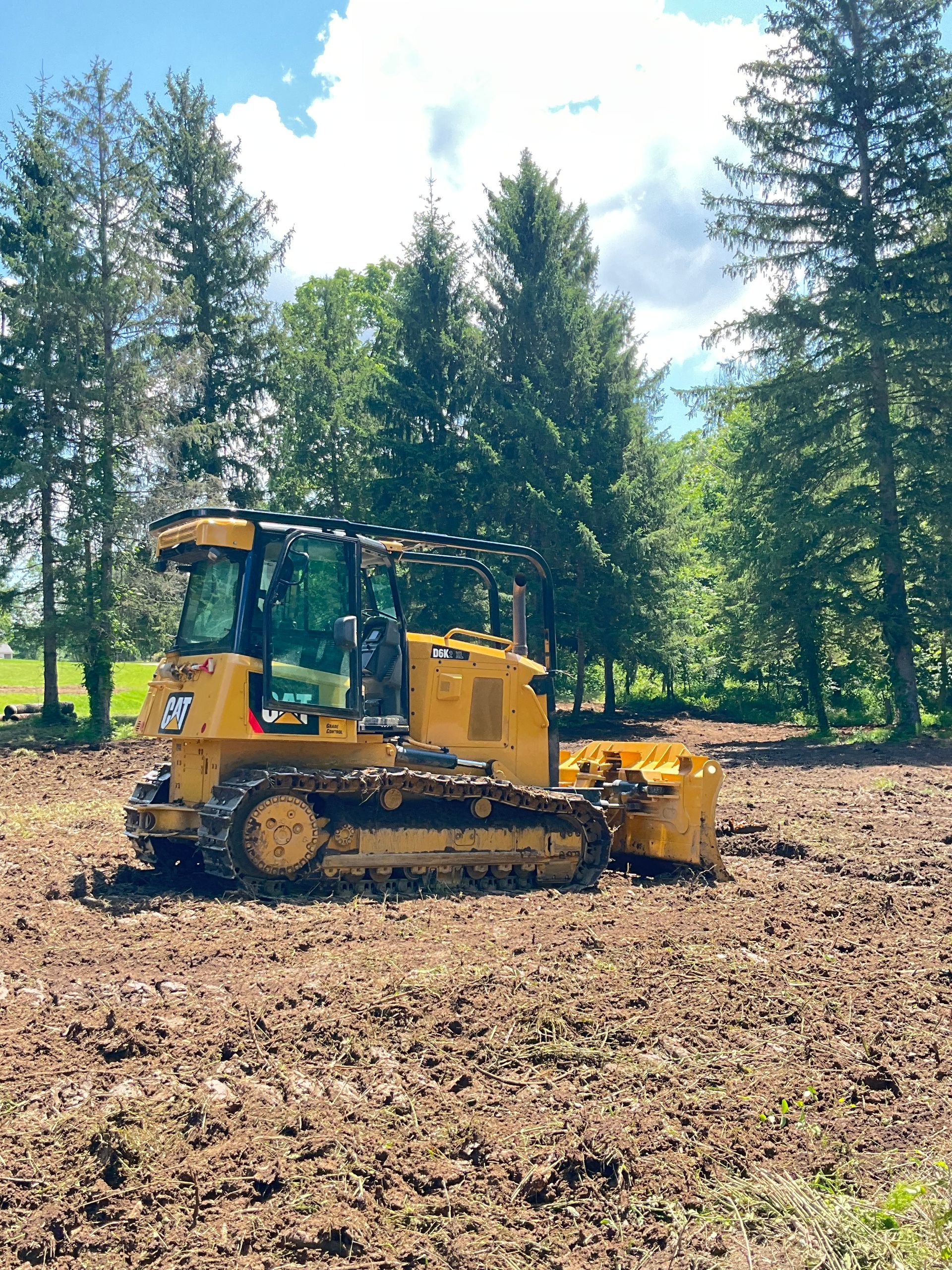 Yellow excavator on a dirt ground, near a pile of rocks and trees.