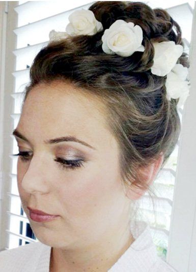 A woman with white flowers in her hair in a bun and professional makeup.