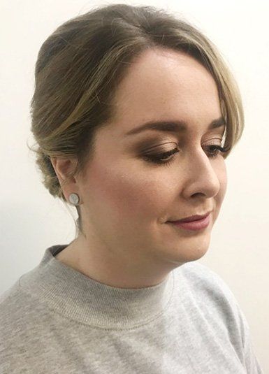 A close up of a woman wearing a grey sweater and earrings with professional makeup.