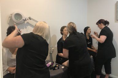 A group of women are getting their makeup done at a table in a room.