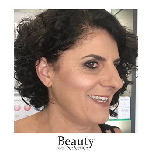 A woman with curly hair is smiling and wearing makeup.