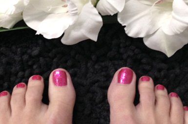 A woman 's feet with pink nails and white flowers in the background.