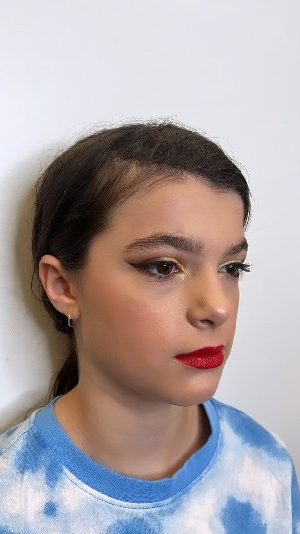 A young girl wearing a blue tie dye shirt and red lipstick.