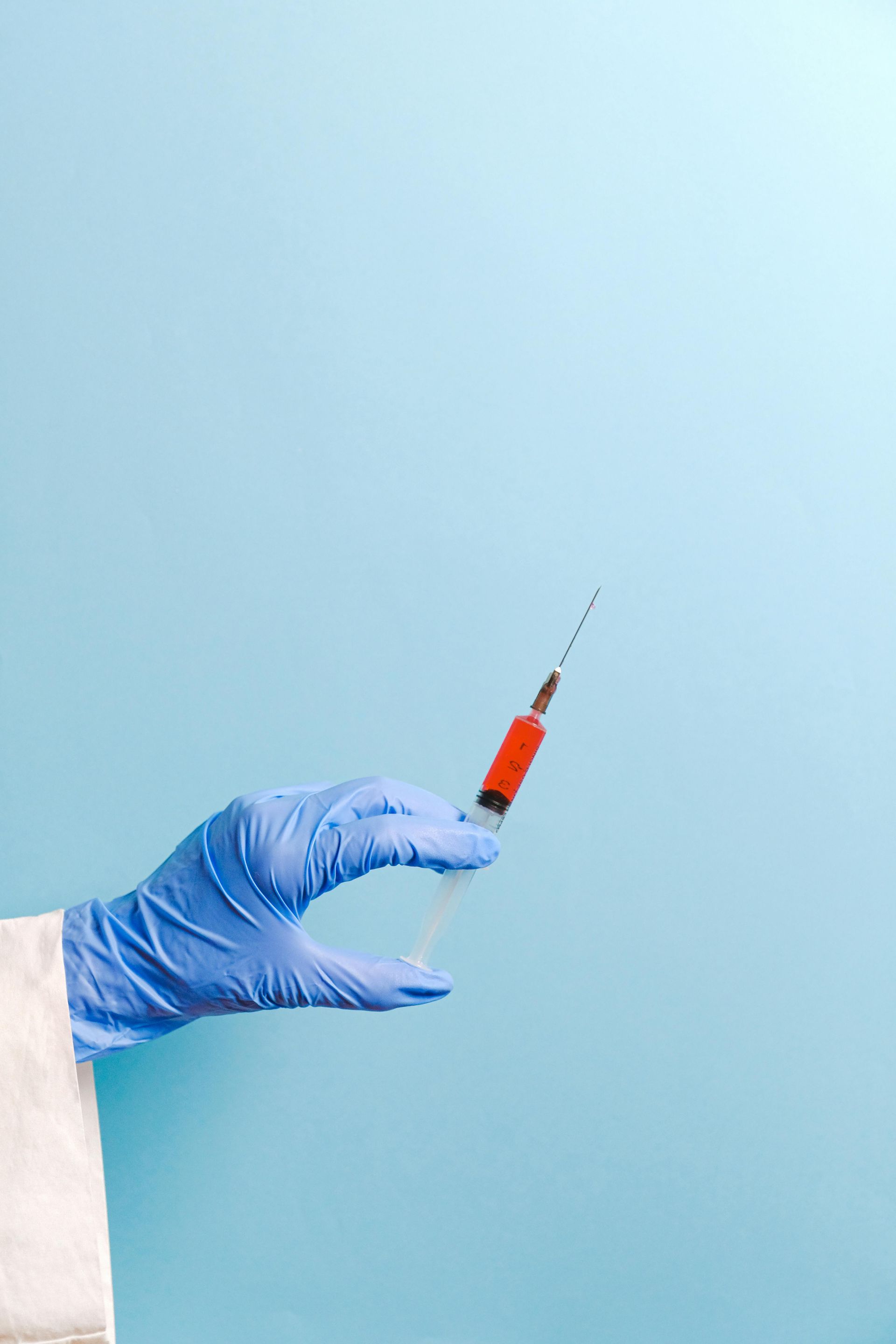 A hand in a blue glove is holding a syringe on a blue background.