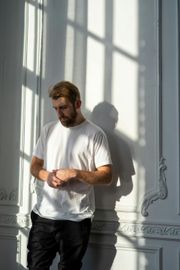 A man in a white t-shirt is standing in front of a window.